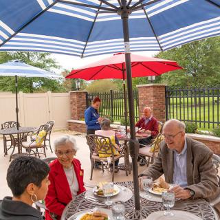 A group of people enjoying a meal together on an outdoor patio under large umbrellas.