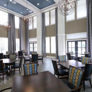 A modern dining room with high ceilings and large windows, featuring elegant chandeliers and stylish furniture.