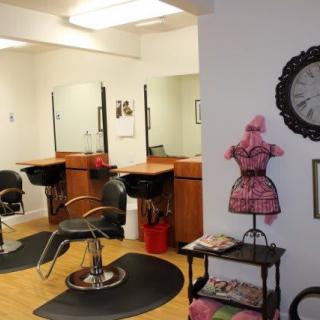 A cozy hair salon with styling stations, mirrors, and a waiting area adorned with a decorative mannequin and clock.
