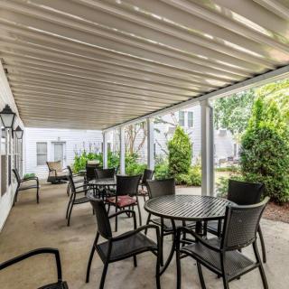 A covered patio with tables and chairs, surrounded by lush greenery.