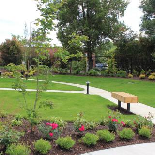 A beautifully landscaped garden with a pathway and benches surrounded by lush greenery and vibrant flowers.