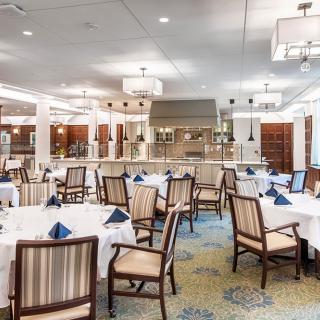 An elegant restaurant dining room with neatly arranged tables and chairs, adorned with white tablecloths and blue napkins.