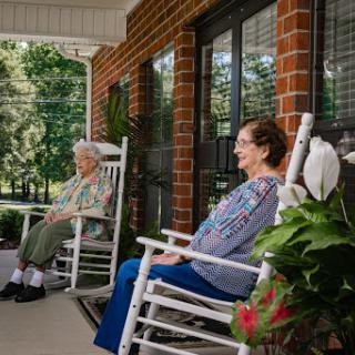Two elderly women enjoying a serene moment on the porch in rocking chairs, surrounded by nature.