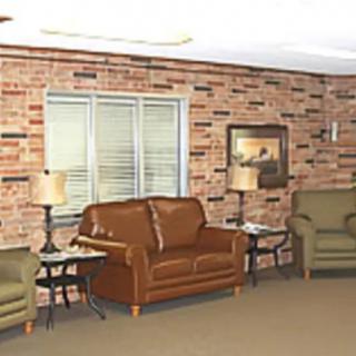 A cozy living room with a brown sofa, armchairs, and a brick wall.
