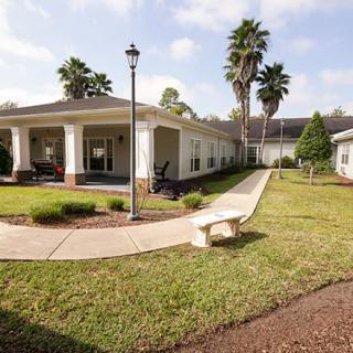 A peaceful outdoor area featuring a pathway leading to a building, surrounded by palm trees and greenery.