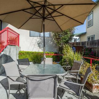 A sunny backyard patio with a table, chairs, and an umbrella surrounded by plants.