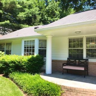 A cozy house with a front porch, featuring a bench and surrounded by lush greenery.
