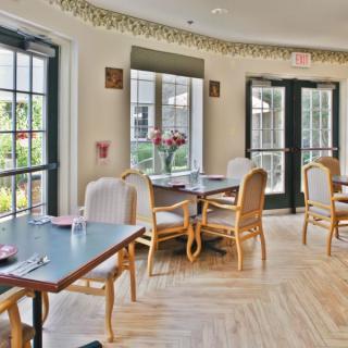 A bright and inviting dining area with several tables and chairs arranged near large windows letting in natural light.