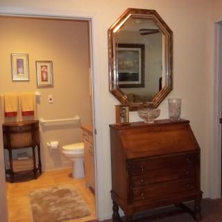 A cozy interior view featuring a bathroom with wall art, a wooden cabinet with an octagonal mirror above, and decorative elements.