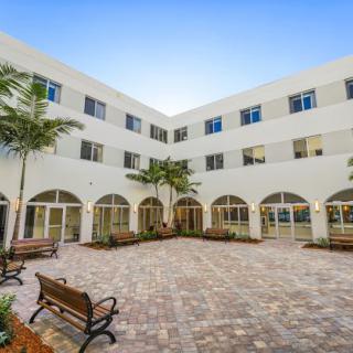 A serene courtyard featuring benches, palm trees, and a building with arched windows.