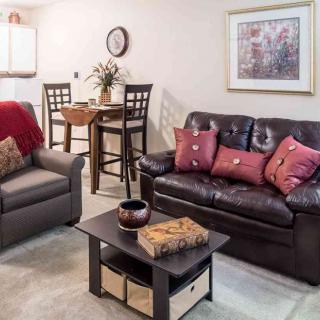 A cozy living room with a sofa, armchair, and coffee table, adjacent to a small dining area.