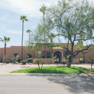 A desert-style house with palm trees and a lush front yard on a sunny day.