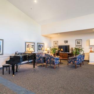 A spacious living room featuring a grand piano, comfortable seating, various artworks, and indoor plants.