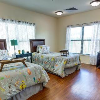 A cozy bedroom with twin beds, featuring ample natural light and warm wooden flooring.