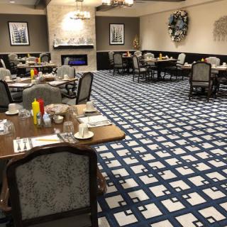 An empty dining room with neatly arranged tables and chairs, featuring a patterned carpet and elegant decor.