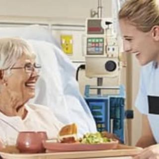 A nurse engages warmly with an elderly patient in a hospital setting, delivering a meal.