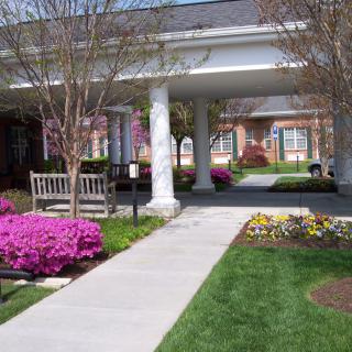 A well-maintained garden with a walkway, colorful flowers, benches, and surrounding architecture.