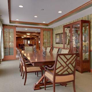 An elegant dining room with a long wooden table, upholstered chairs, and a glass-front china cabinet.