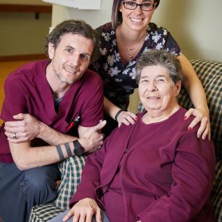 A group of three people, including an elderly woman, smiling together indoors.