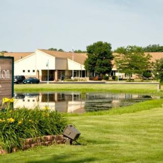 A building with a pond and landscaped surroundings, featuring a grassy area and trees.
