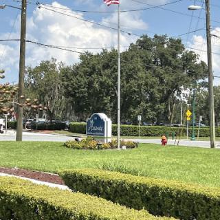 A view of a landscaped area featuring a flag and signage, with trees and a clear sky.