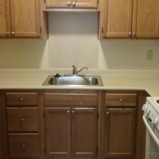 A small kitchen area with wooden cabinets, a stainless steel sink, and an adjoining stove.