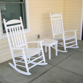 Two white rocking chairs and a small table on a porch.