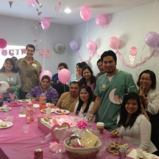 A group of people celebrating a baby shower with pink decorations and balloons.