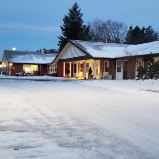 A peaceful winter evening scene with snow covering the ground and warm lights illuminating the buildings.