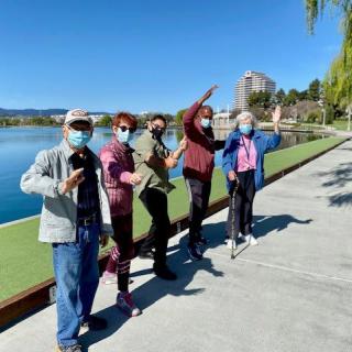A group of people wearing masks enjoying a sunny day by the lake.