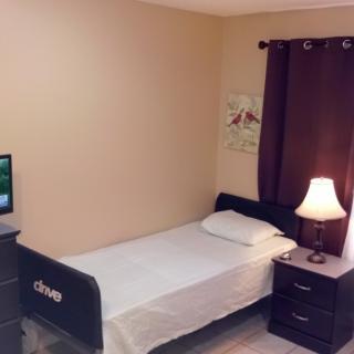A cozy bedroom with a single bed and nightstand, adorned with a lamp and small television.