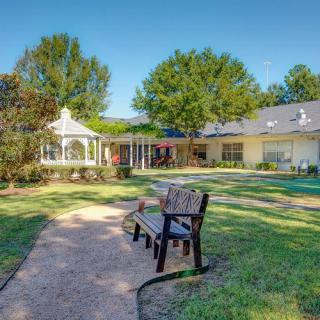 A peaceful garden with a bench and gazebo on a sunny day.