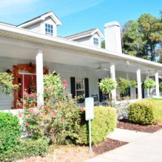 A bright and sunny view of a house with a spacious porch, surrounded by landscaped greenery.