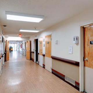 A clean and well-lit hospital hallway, lined with doors leading to different rooms.