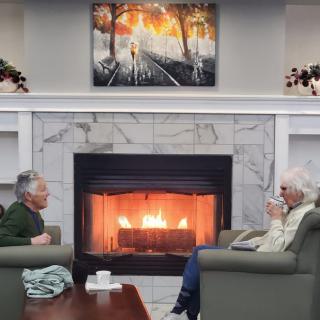 Two people enjoying a conversation by the warm fireplace in a cozy living room setting.