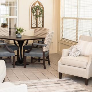 A cozy living room featuring a dining area with a round table and chairs, an armchair, and decorative elements including plants and window blinds.