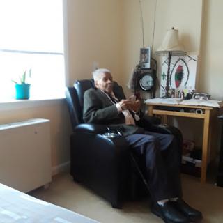 An elderly man sitting comfortably in a chair, enjoying his surroundings in a cozy living space.