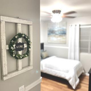 A cozy and stylish bedroom featuring a decorative wreath on the wall and a neatly made bed, illuminated by natural light.