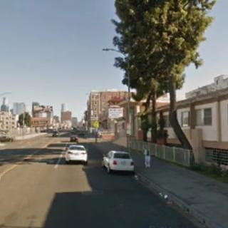 An urban street scene with parked cars and buildings under a clear sky.
