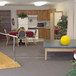 A rehabilitation room with exercise equipment, a kitchen area, and seating.