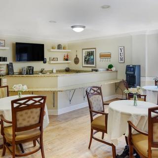 A cozy cafe interior with neatly arranged tables and chairs, featuring a bar counter and a television.