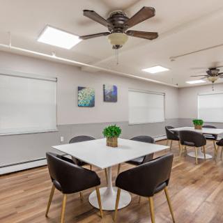 A modern meeting room equipped with comfortable chairs, tables, and ample natural light.
