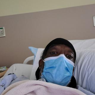 A person wearing a face mask is resting in a hospital bed.