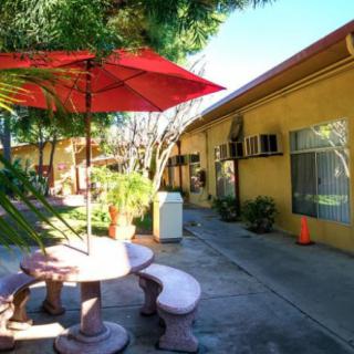 A courtyard with a picnic table and red umbrella, surrounded by greenery and buildings.