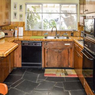 A cozy kitchen interior featuring wooden cabinets, a dishwasher, an oven, and a large window.