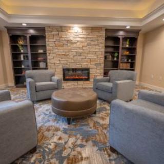 A cozy living room with a central fireplace, surrounded by comfortable armchairs and shelves.