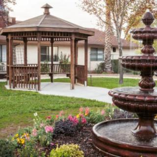 A serene garden scene featuring a wooden gazebo and a tiered fountain surrounded by flowers.