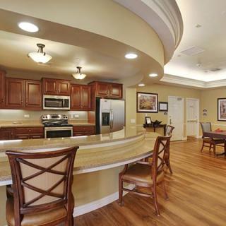 A modern kitchen with wood flooring and stainless steel appliances, featuring a curved bar and dining area.
