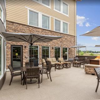 A comfortable outdoor patio with tables, chairs, and umbrellas, adjacent to a building under a clear blue sky.