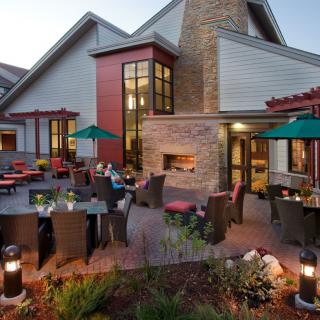 A modern outdoor patio area with seating and a fireplace, set against an evening backdrop.